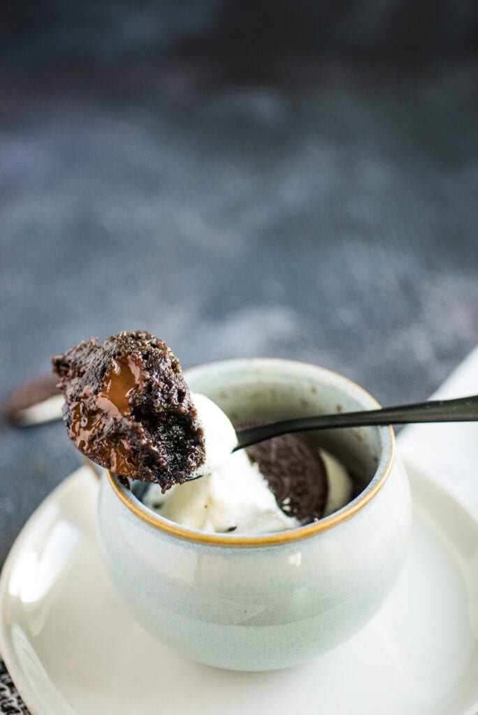 Close-up bite of Oreo Mug Cake in a spoon resting on a coffee mug