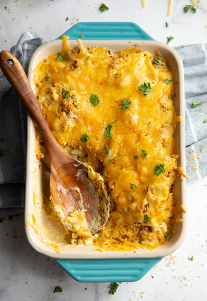 Baked Macaroni and Cheese in a teal baking dish with a wooden spoon resting in the dish
