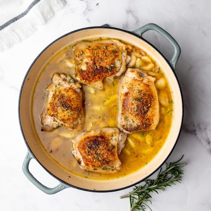 Chicken thighs in a garlic white wine sauce in a cast iron enamel pan